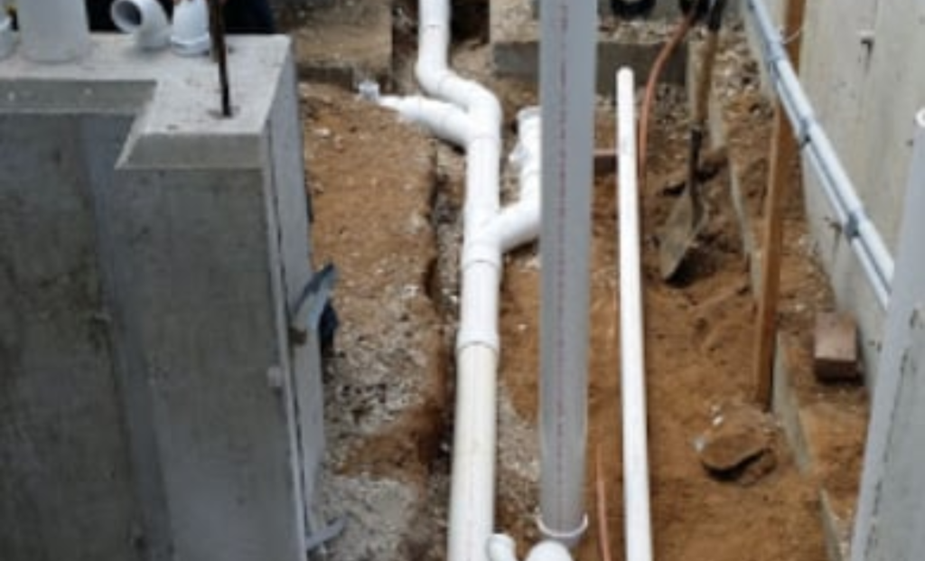 Concrete basin and white PVC pipes in an excavated trench