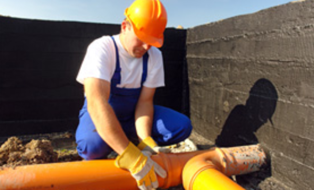 Plumber in a hard hat fitting an orange PVC sewer pipe