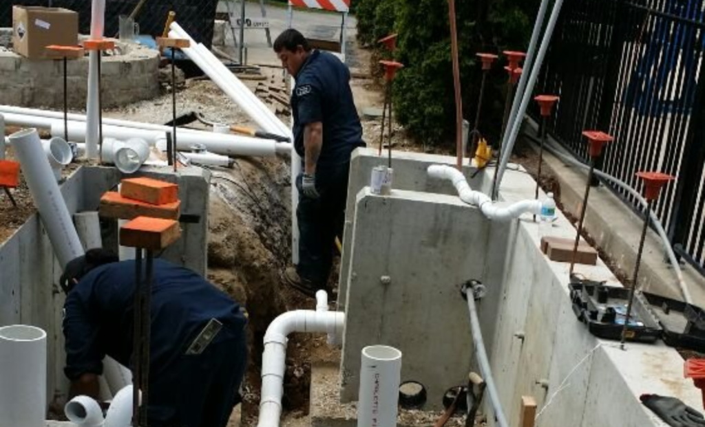 Excavated basin with white PVC pipes beside a building foundation