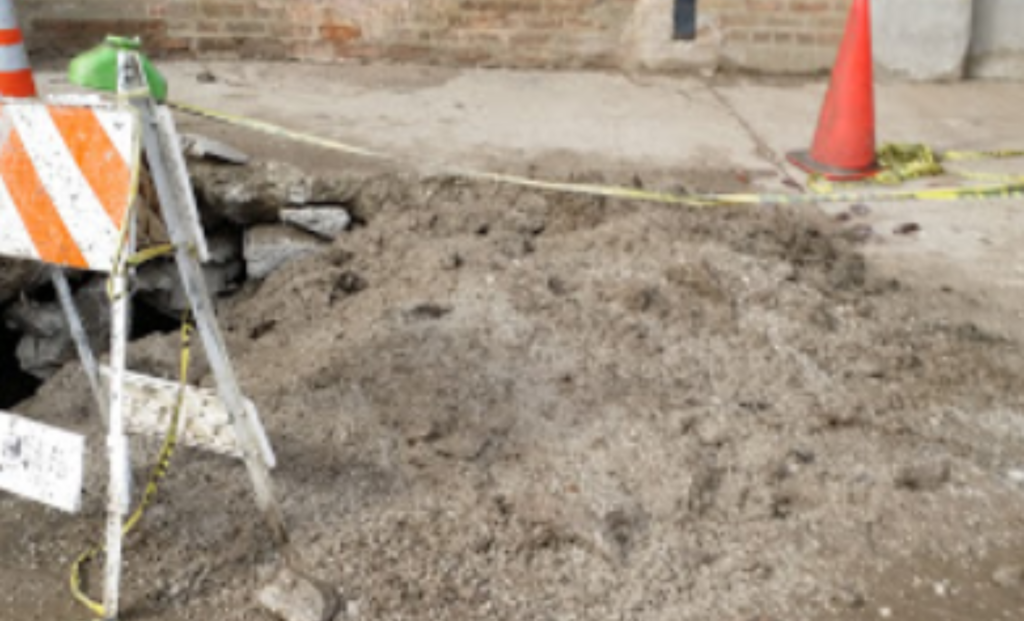 Excavated yard with a traffic cone at a sewer repair site
