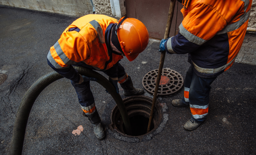 Crew in safety gear clearing a street drain with a hose